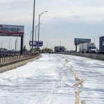 White tarp covers part of the I-294 Bensonville bridge in Chicago, IL, as traffic drives past concrete barriers.