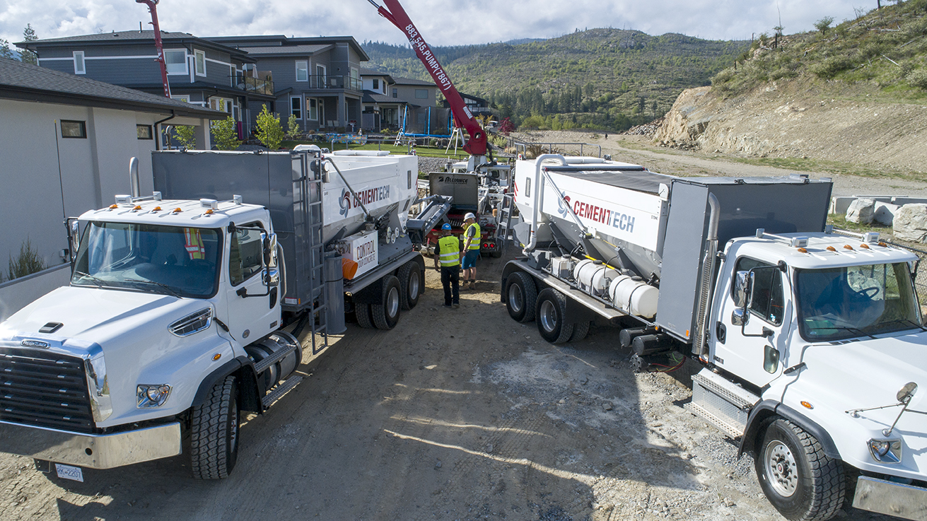 2 volumetric mixers from Joe & Sons Concrete pour volumetric concrete into a concrete pump on a jobsite in Kelowna, B.C.