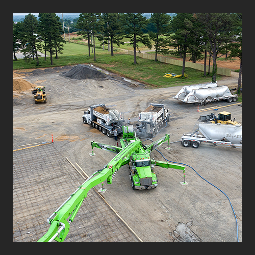 Drone photo of 2 volumetric mixers pouring concrete into a concrete pump for a continuous pour in Poteau, OK.